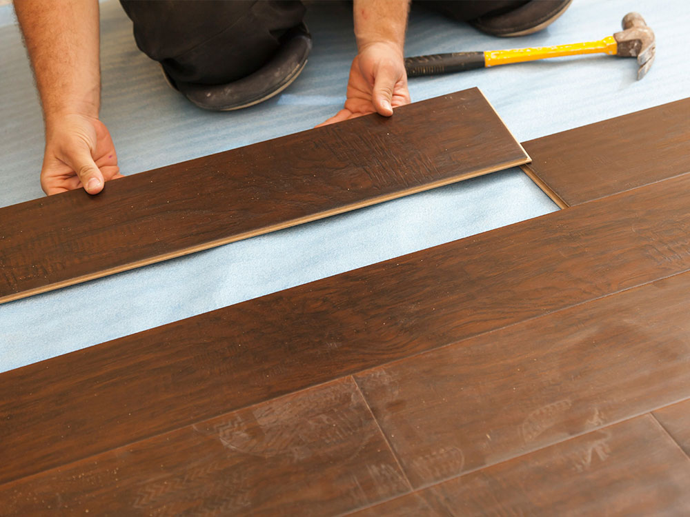 Tradesperson installing dark wood laminate flooring as part of commercial and residential flooring supply services