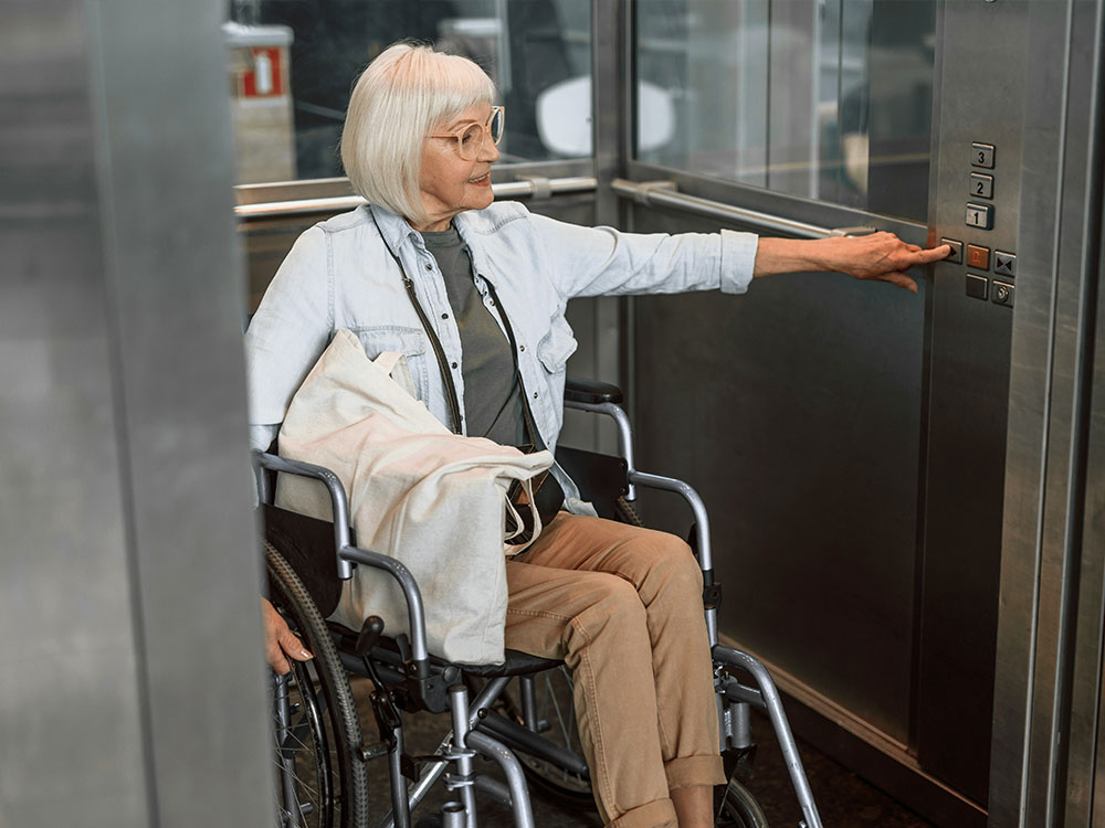 Senior resident in a wheelchair pressing a floor button inside an accessible platform lift