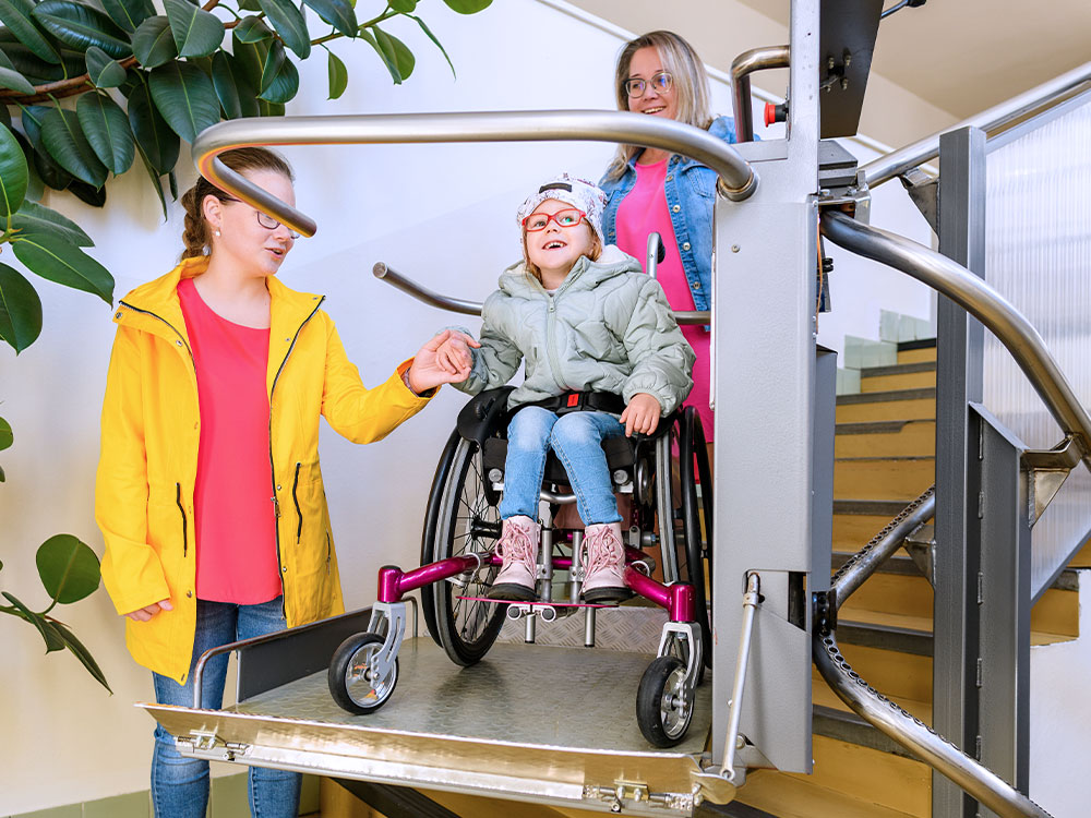 Child in a wheelchair using an inclined platform stairlift with support from adults