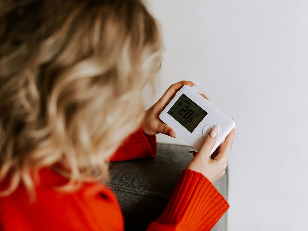 Resident adjusting a smart digital room thermostat to improve home energy efficiency and decarbonisation