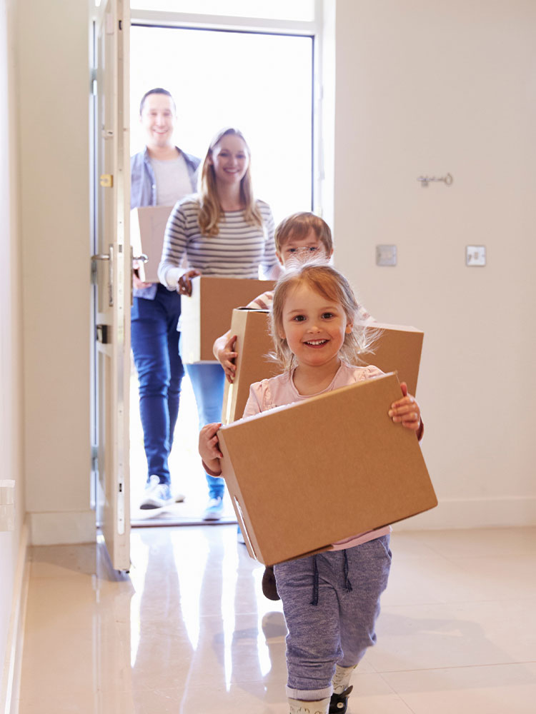 Young family carrying moving boxes through the front door of their new build house